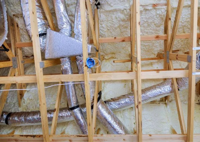 HVAC duct system with flexible insulated tubing installed in a home under construction, surrounded by wooden framing and spray foam insulation.