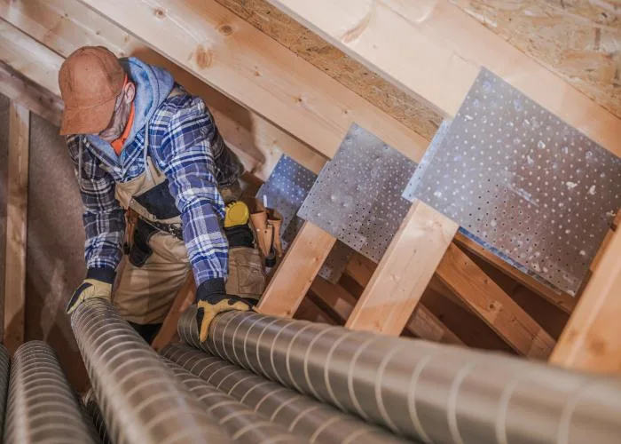 HVAC technician installing ductwork in an attic space, securing ventilation pipes for proper airflow.